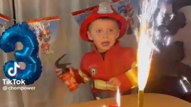 Niño vestido de bombero se asusta con la vela de su pastel de cumpleaños