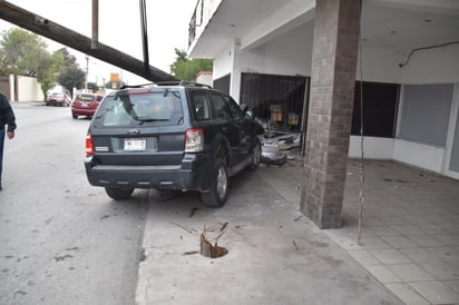 Vehículo tumba poste y cae en fachada de un despacho