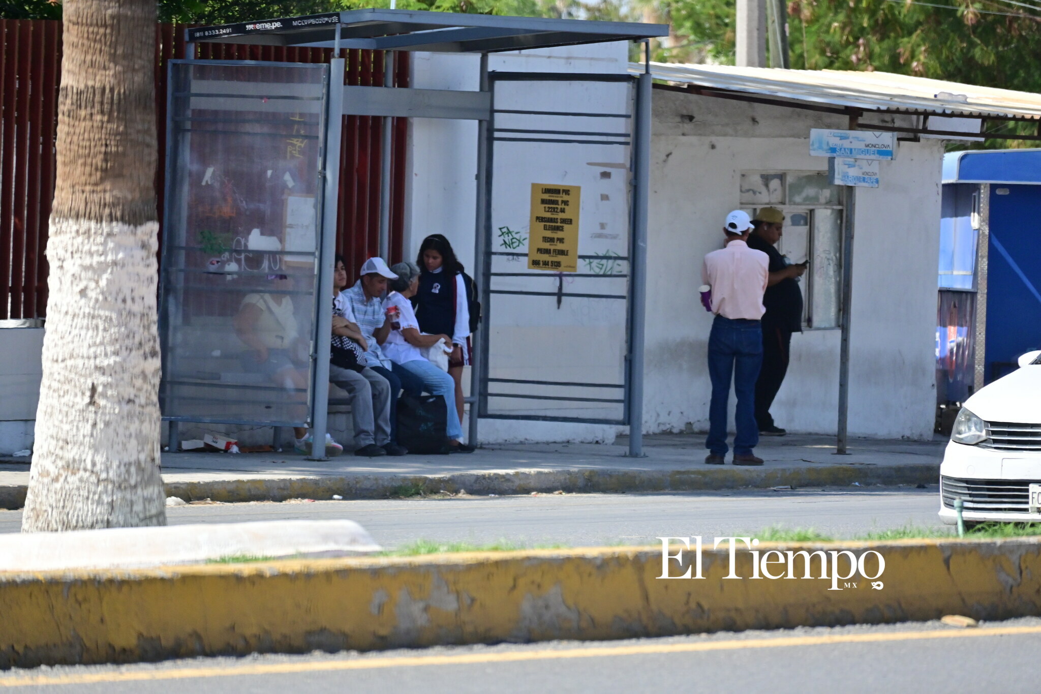 Ciudadanos intentan mitigar el calor y la espera bajo la sobra de un parabus.