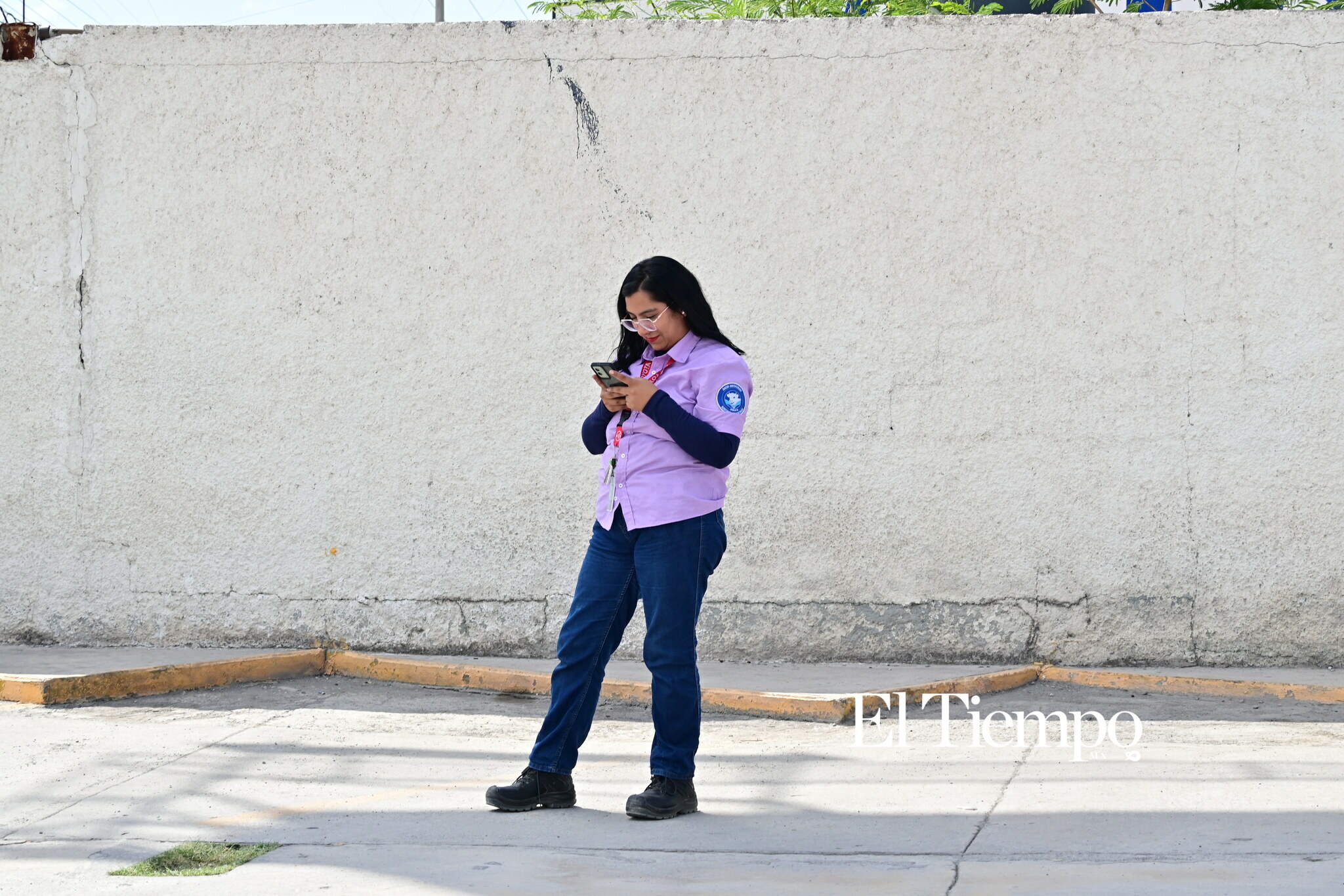 Bajo la sombra, una mujer espera mientras consulta su teléfono celular durante su recorrido por la ciudad.